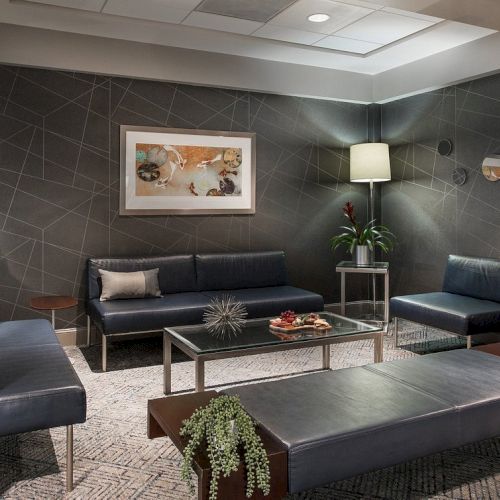 The image shows a modern waiting room with sleek seating, plants, a painting, and soft lighting, creating a relaxing atmosphere.