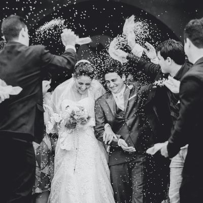 A couple is walking through a group of people throwing confetti, likely celebrating a wedding.