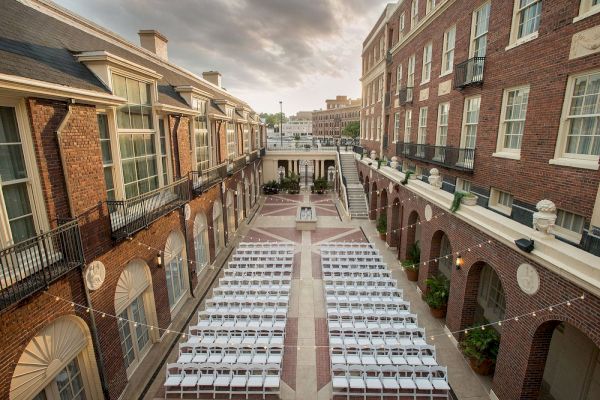 It's an outdoor venue set up for an event, with rows of white chairs between brick buildings under string lights, amidst a courtyard.