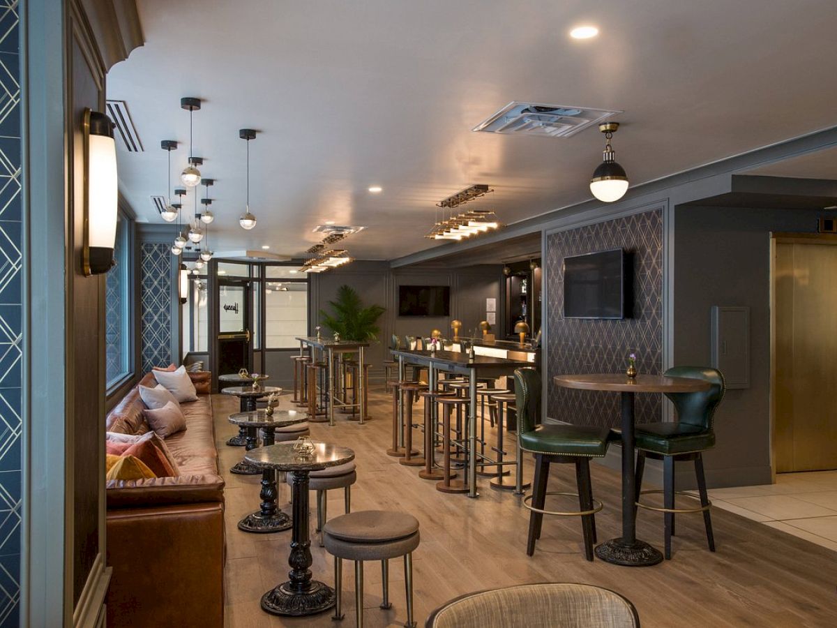 The image shows a stylish bar with modern decor, featuring tables, chairs, and warm lighting in an inviting atmosphere.