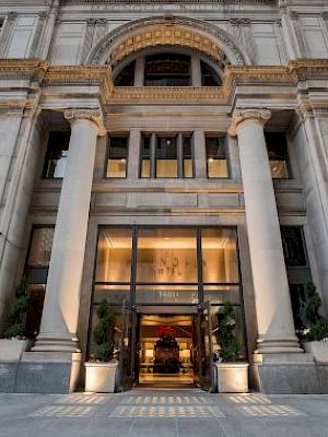 A grand building facade with tall columns, large glass entrance, and decorative arches, located on a city street.