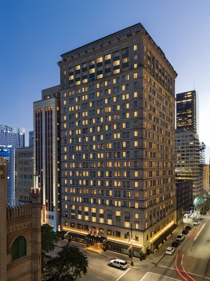 A tall, well-lit building in an urban cityscape at dusk, with visible street and surrounding skyscrapers.