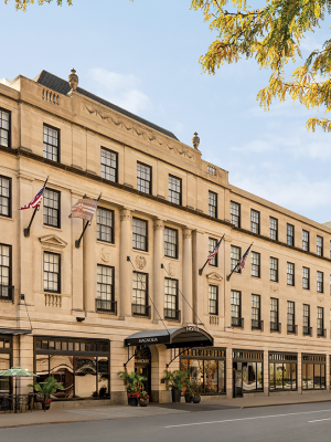 The image shows a classic multi-story building with flags, awnings, and street-level entrances on a sunny day.