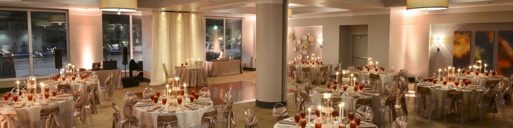 Elegant banquet hall set for an event with round tables, white linens, ribbon-tied chairs, and glowing candles creating a warm ambiance.