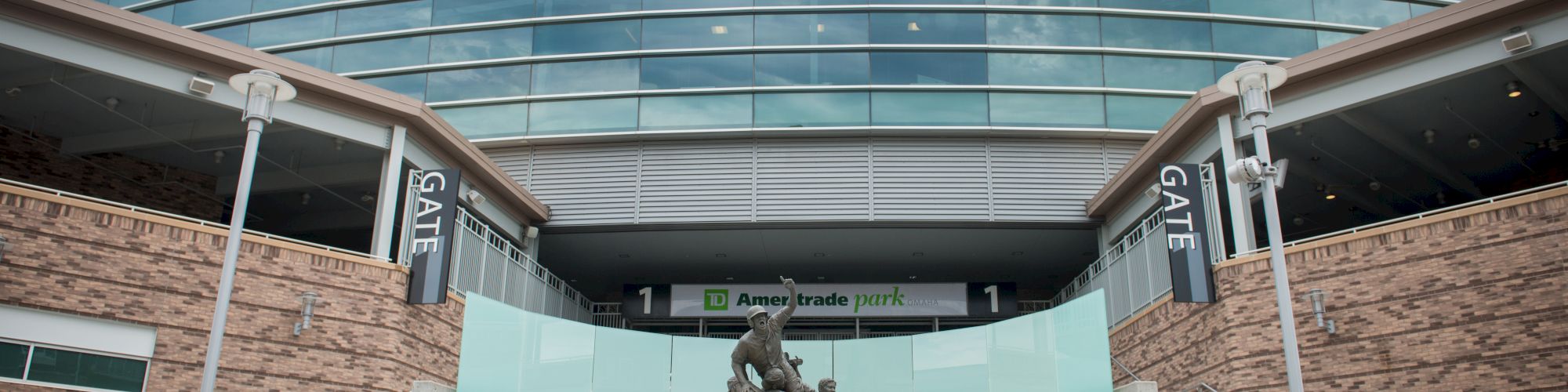 The image shows the entrance of TD Ameritrade Park in Omaha, featuring a prominent statue and the stadium's signage.