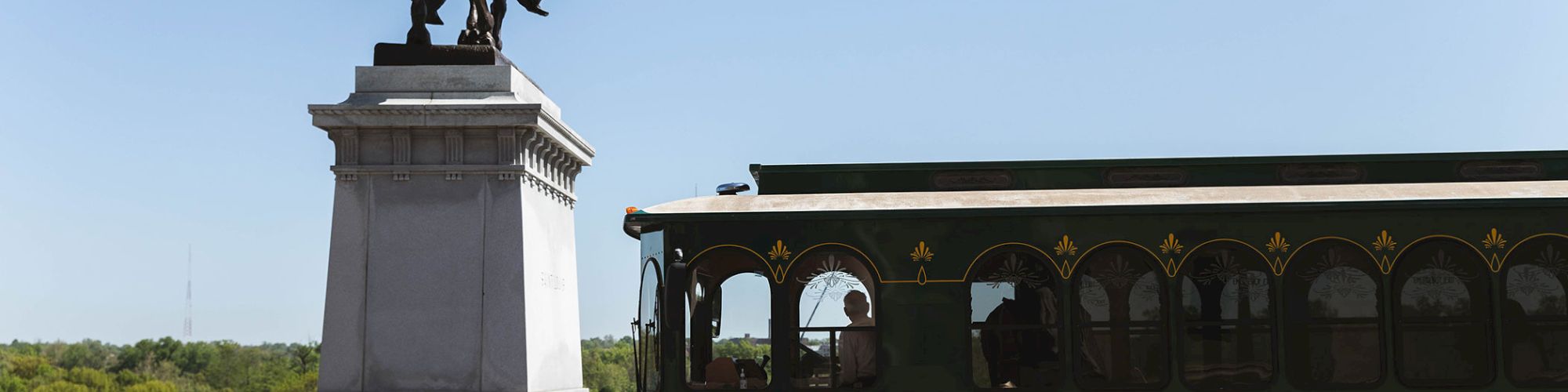 A statue of a rider on a horse stands beside a parked red trolley labeled 