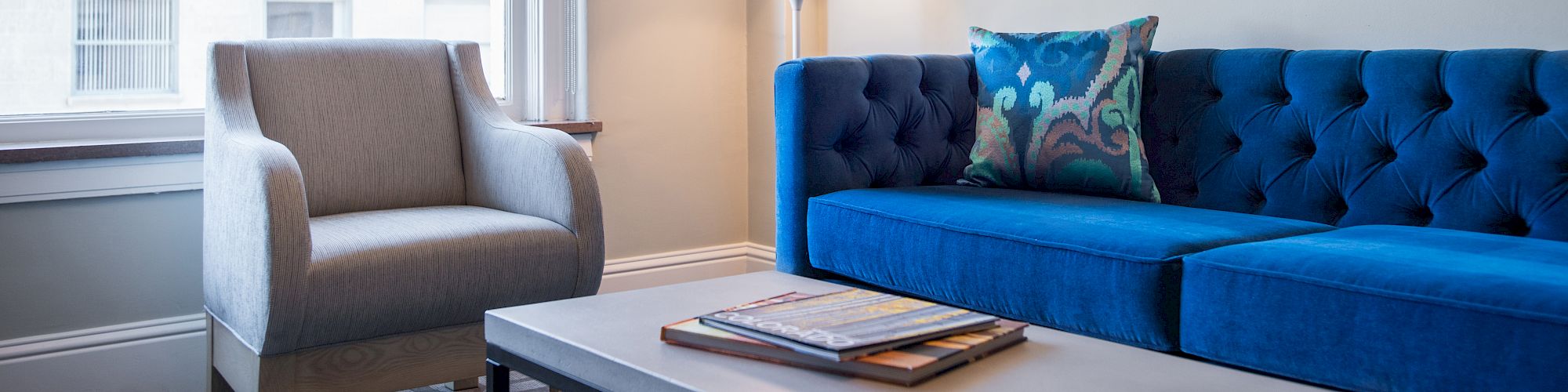 A modern living room with a blue couch, armchair, coffee table, lamp, and framed pictures on the wall.