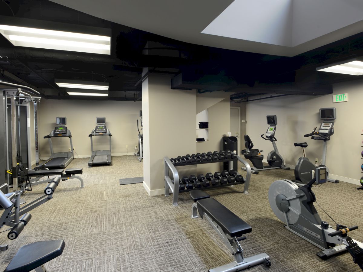 A gym with treadmills, stationary bikes, rowing machine, weight benches, dumbbells, and colorful exercise balls is shown.