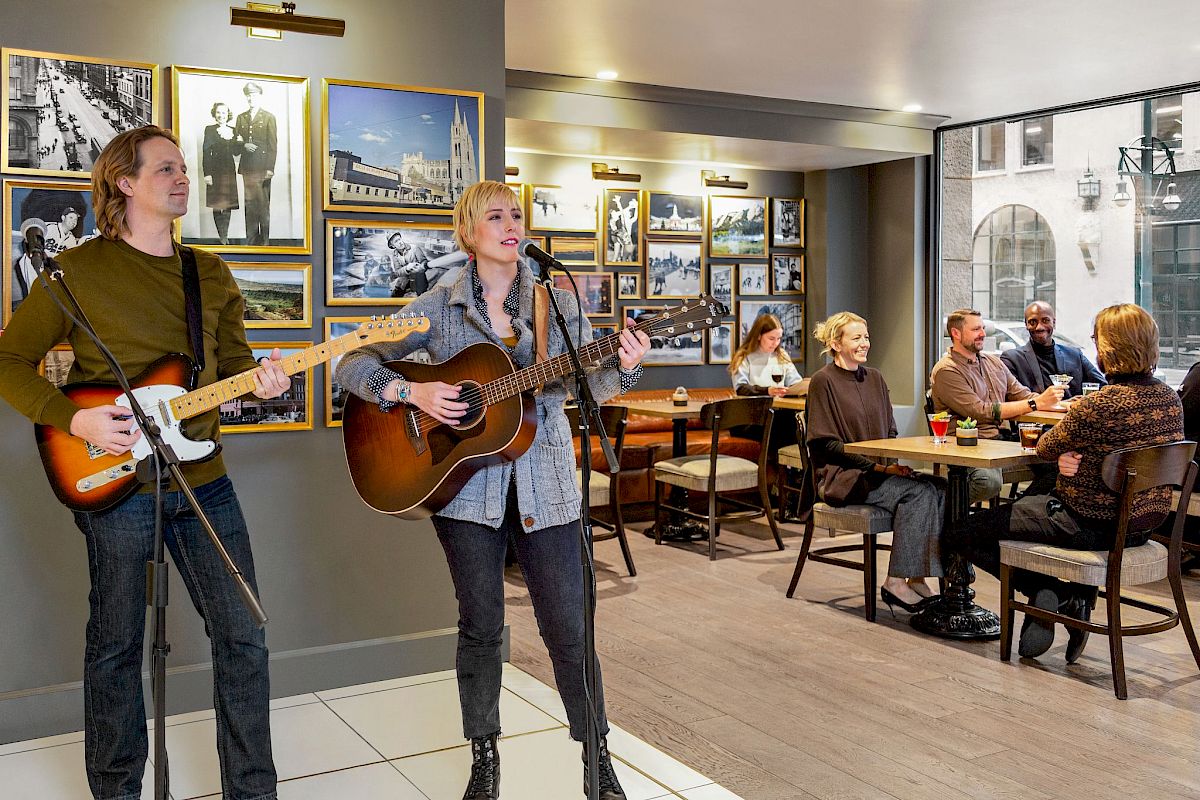 Two musicians are performing with guitars in a café. People sit at tables, enjoying the music and the atmosphere.