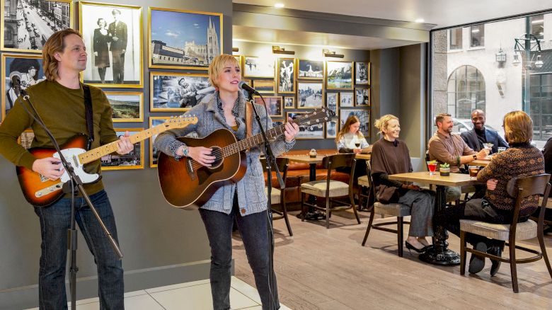 Two musicians are performing with guitars in a café. People sit at tables, enjoying the music and the atmosphere.