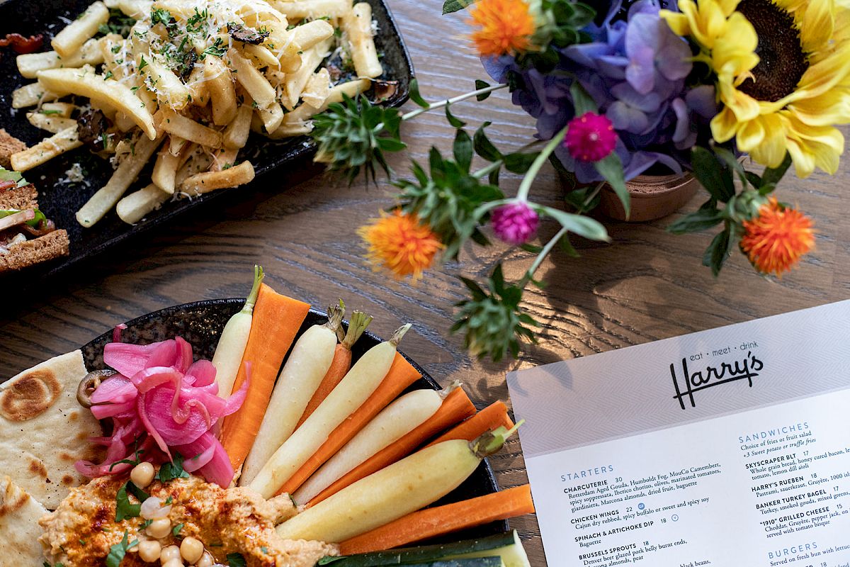 A table setting with fries, a veggie platter, a menu, and vibrant flowers in a vase.