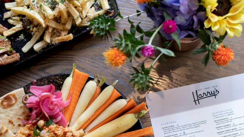 A table setting with fries, a veggie platter, a menu, and vibrant flowers in a vase.