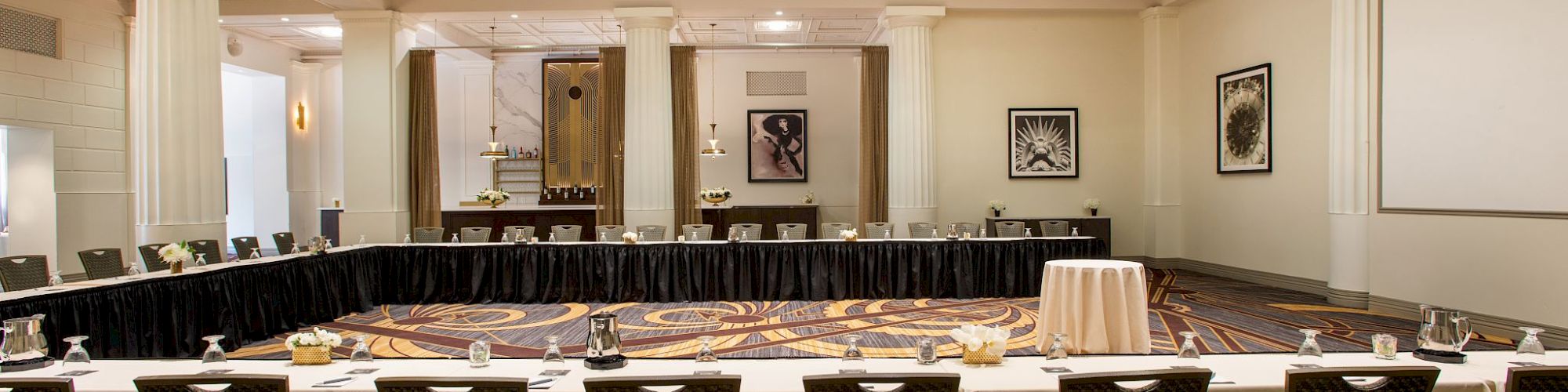 A conference room with a rectangular U-shaped table setup, surrounded by chairs, under a large skylight, with art on the walls.