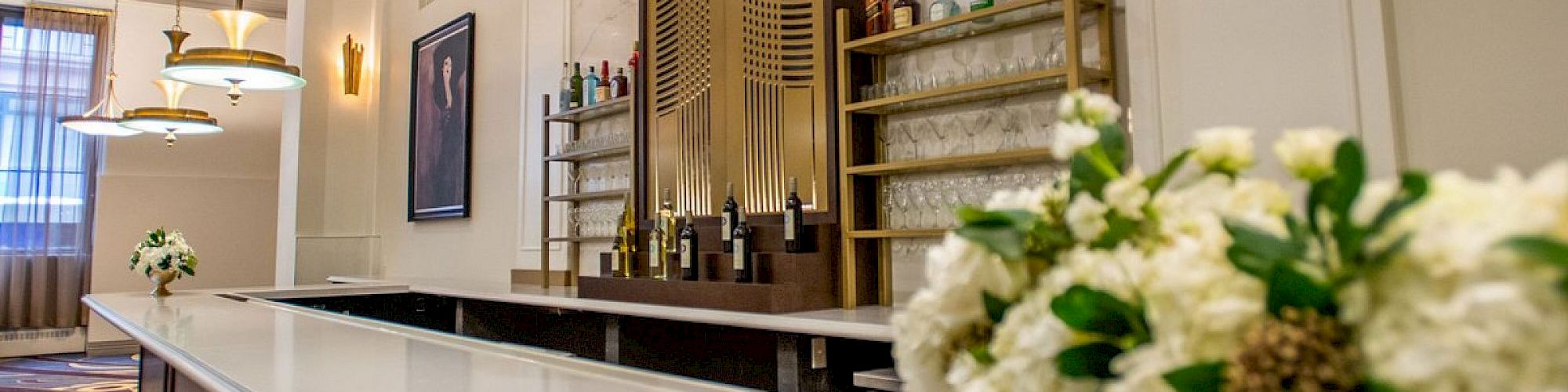 An elegant bar with floral decorations, stylish lighting, and neatly arranged bottles on shelves in a modern, sophisticated setting.