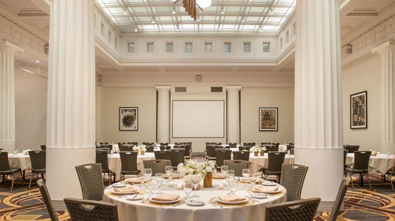 A banquet hall with a round table set for an event, featuring elegant decor and a chandelier.