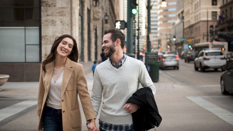 A couple is walking hand in hand on a city street, smiling and enjoying each other's company.