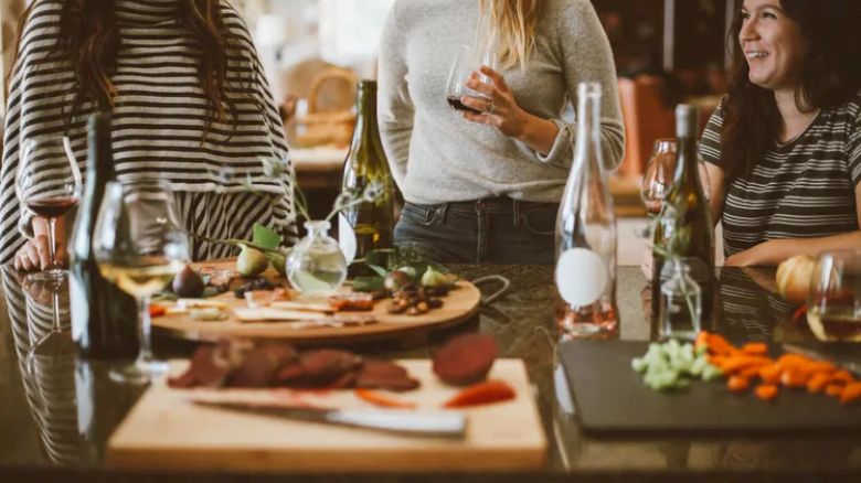 People enjoy wine and appetizers around a table, with various dishes and bottles present.