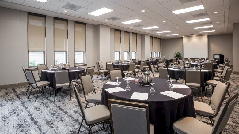 The image shows a conference room set with round tables, chairs, paper, and glasses, ready for an event or meeting.