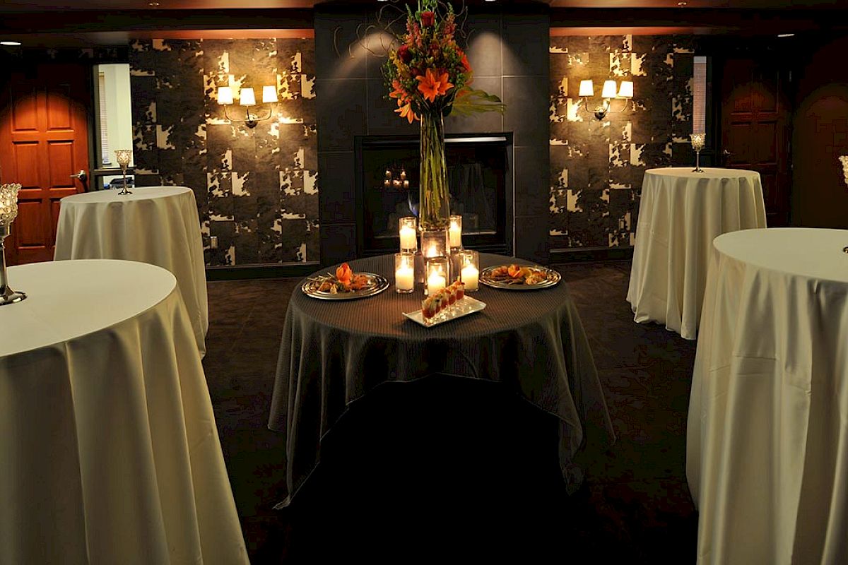 A dimly lit room set for an event with round tables, candles, floral arrangements, and hors d'oeuvres.