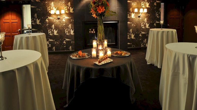 A dimly lit room set for an event with round tables, candles, floral arrangements, and hors d'oeuvres.