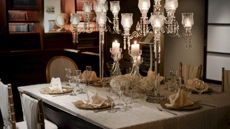 A dining table elegantly set with crystal chandeliers, wine glasses, and folded napkins, creating a luxurious and inviting ambiance.