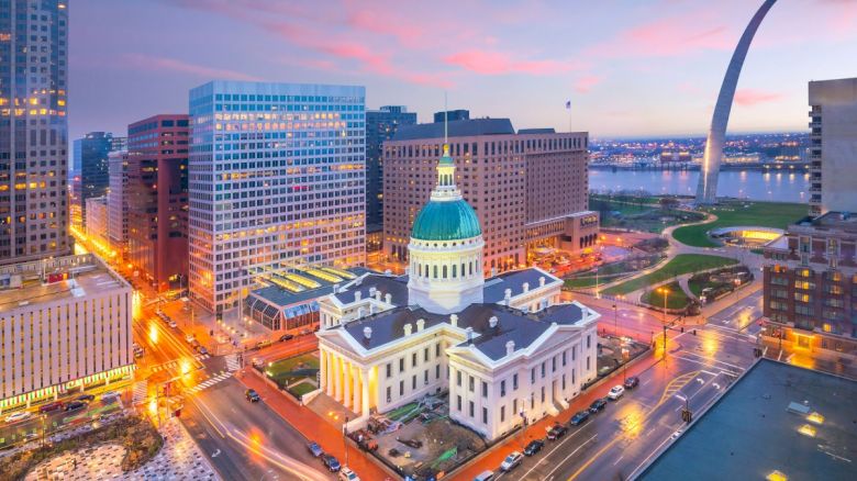 This image shows a cityscape with a historic domed building, surrounded by modern skyscrapers, and the Gateway Arch by the river at sunset.