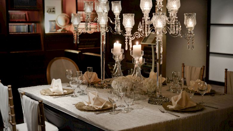 A elegantly set dining table with ornate candle holders, folded napkins, glassware, and plates, creating a sophisticated dining atmosphere.