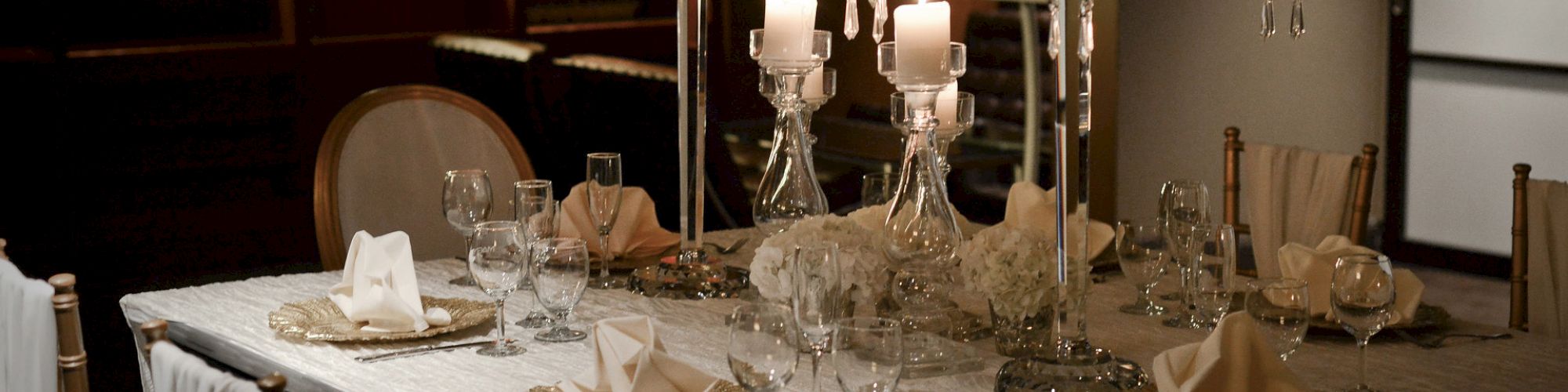 An elegantly set dining table with ornate candelabras, folded napkins, glassware, and china, in a warmly lit room with bookshelves.