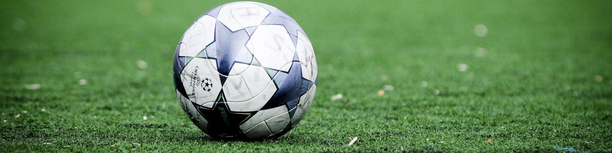 A soccer ball resting on a green artificial turf field, with a blurred background.