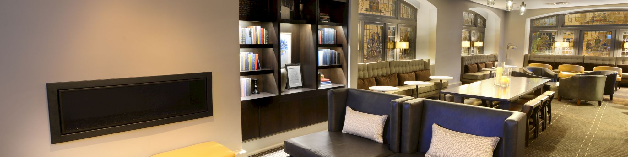 A modern lounge area with black sofas, yellow stools, bookshelves, and ambient lighting, creating a cozy and stylish atmosphere.