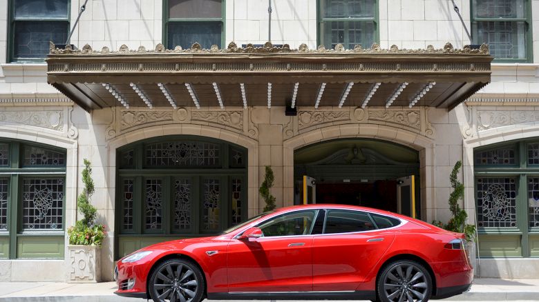 A red car is parked on the street in front of an ornate building with large windows and decorative elements.