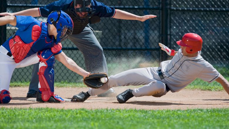 A baseball player slides into home plate as the catcher attempts a tag. An umpire closely watches the play.