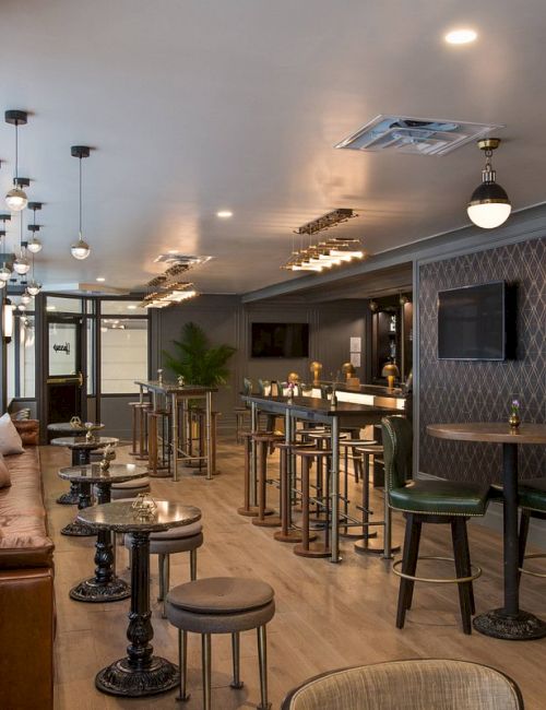 The image shows a stylish bar with high stools, tables, dim lighting, and decorative walls. There's a cozy seating area and an elevator.