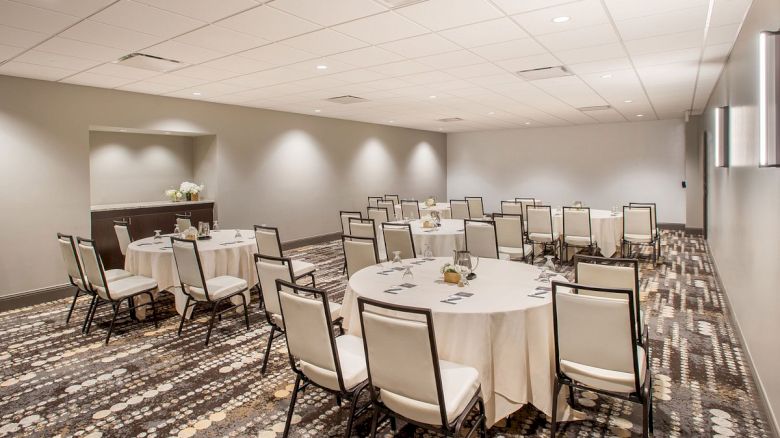 A conference room with round tables and chairs on a patterned carpet, set for a meeting or event, and neutral-colored walls.