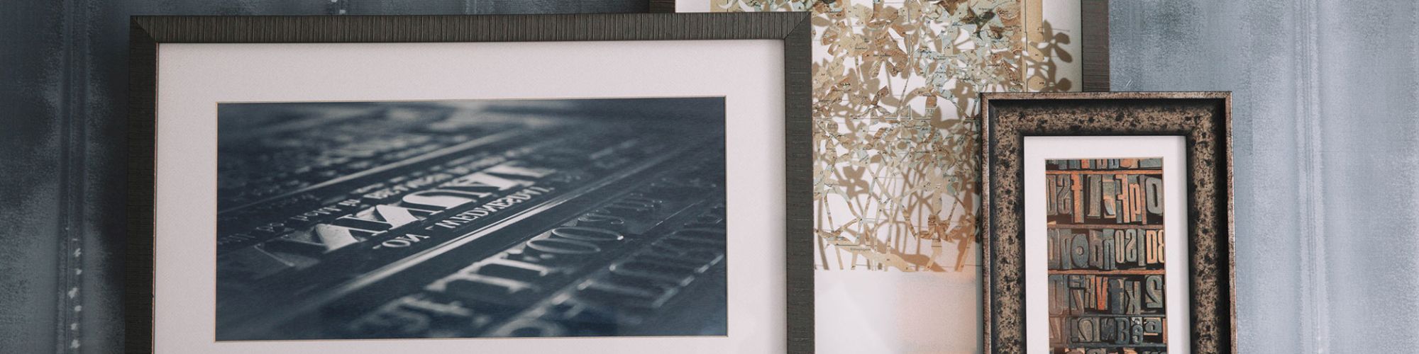 Three framed artworks on a shelf with a textured gray wall background, featuring abstract and natural designs in varying frame sizes.