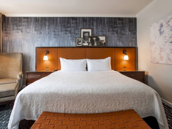 A stylish hotel room with a cozy bed, modern décor, framed photos above, and a textured wall behind the headboard.