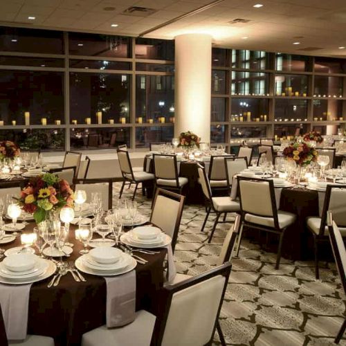 A decorated banquet hall with round tables, elegant place settings, floral centerpieces, and candlelit ambiance creates a sophisticated atmosphere.