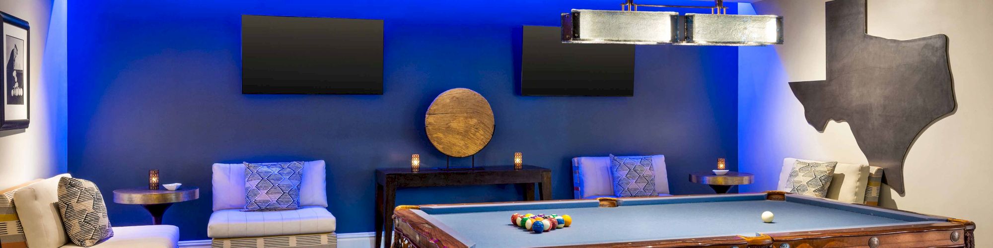 The image shows a stylish game room with a pool table, lounge seating, and a Texas wall decoration.