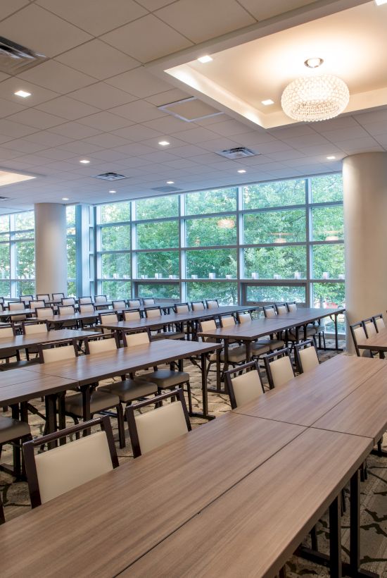 A modern conference room with long tables and chairs, large windows, and bright lighting, ready for an event or meeting.