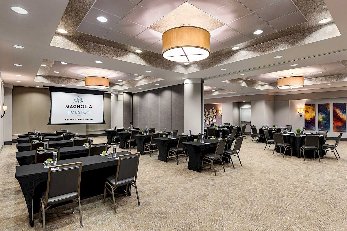 The image shows a conference room setup with tables and chairs, a projector screen displaying