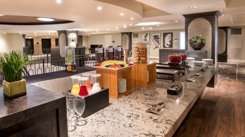 The image shows a buffet setup with drinks, fruits, and cookies on a granite counter in a spacious and well-lit dining area.