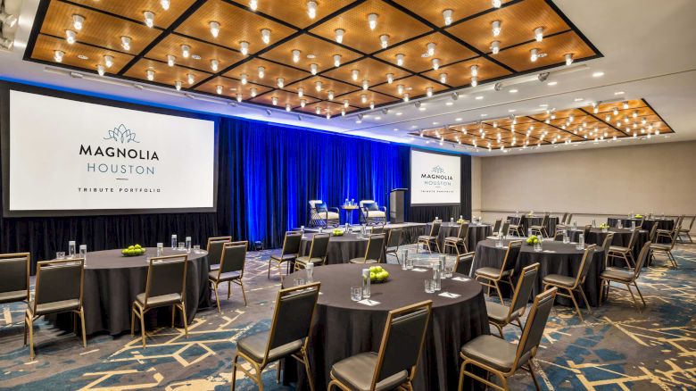 A conference room with round tables, chairs, and large screens displaying 