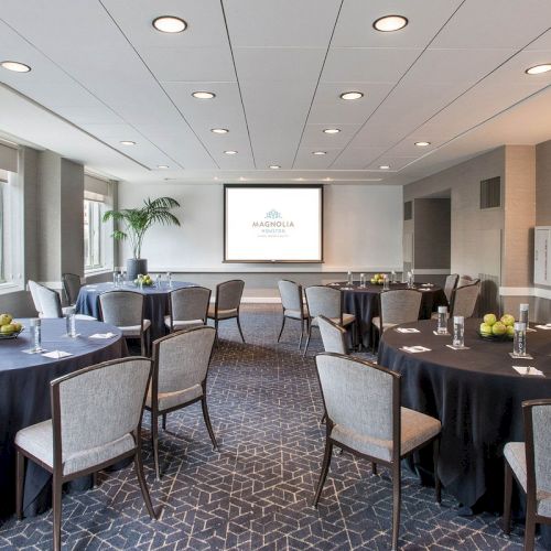 A conference room with round tables and chairs, projector screen, and apples on the tables, set up for a meeting or event.