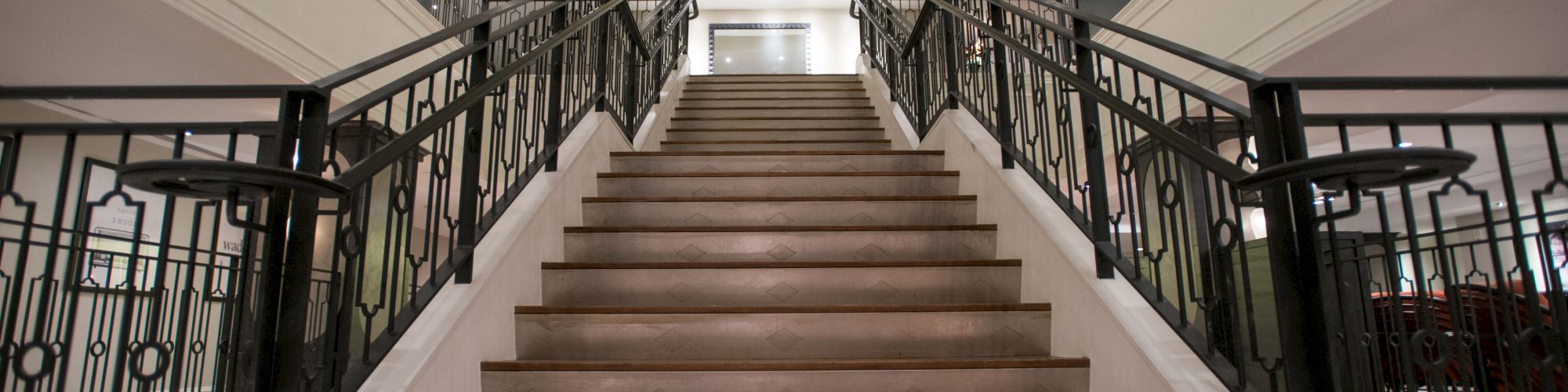 A grand staircase with ornate metal railings leads up to a circular ceiling with soft lighting in an elegant interior setting.