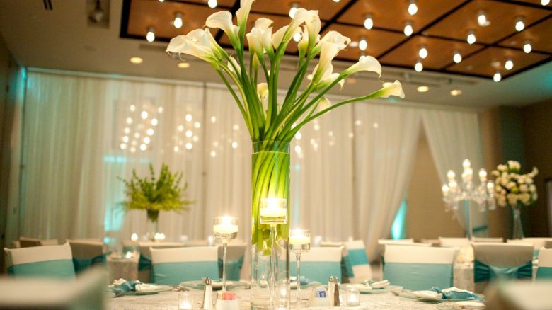 Elegant table setting with white flowers, candles, and teal accents in a softly lit room.