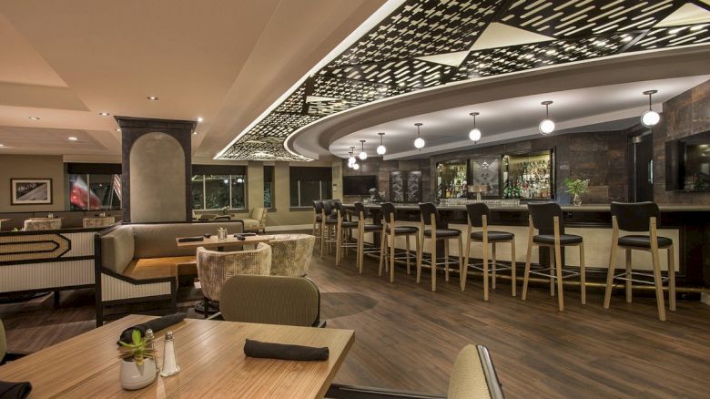 The image shows a stylish restaurant interior with a bar, modern seating, and contemporary design elements, featuring warm lighting and decor.