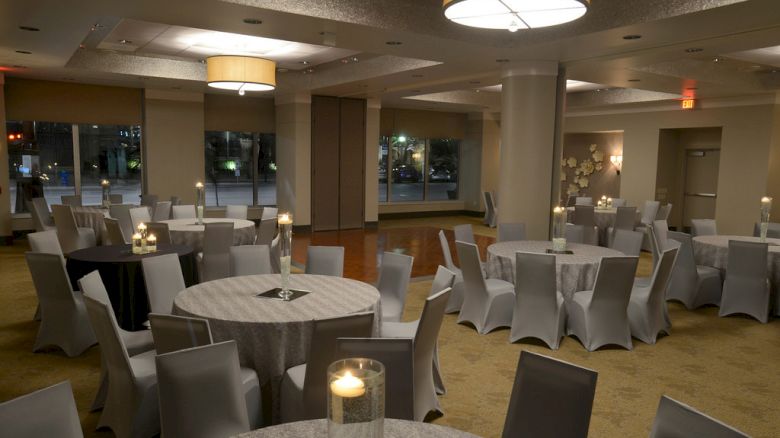 The image shows a well-lit, elegantly decorated banquet hall with round tables, grey covers, and candles on top.