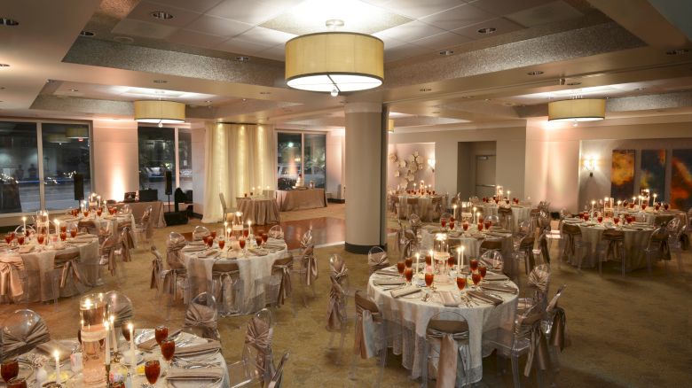 An elegantly decorated banquet hall with round tables, white tablecloths, red drinks, and ambient lighting, ready for an event.