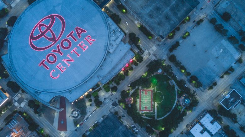 Aerial view of the Toyota Center and surrounding streets at night, with a lit basketball court nearby, in an urban setting.