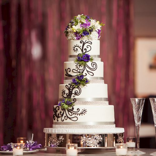 A five-tiered wedding cake with floral decorations, surrounded by candles and two champagne flutes on a table.